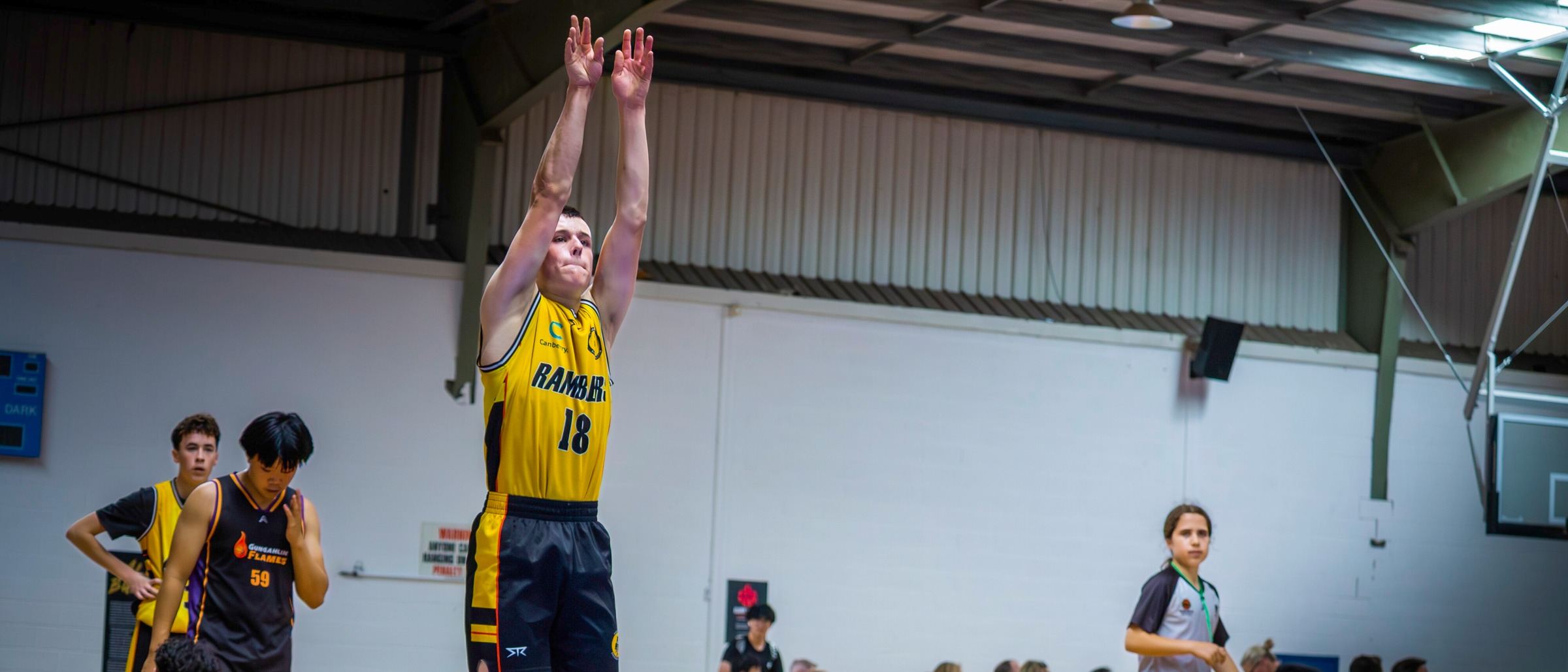 A Ramblers player rises for a jump shot as teammates and the crowd watch on at Belconnen Basketball Stadium